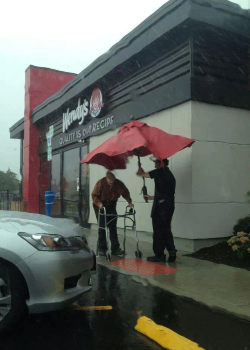 Wendy's Restaurant outside raining employee holding red umbrella for man with a walker